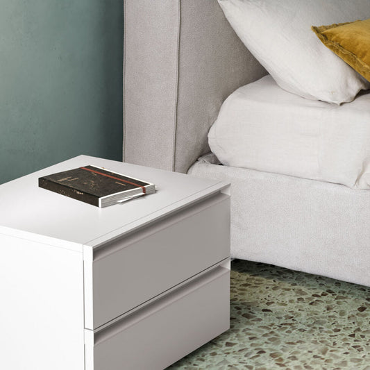 Gray upholstered bed with white bedding and a nightstand with a book against a gray wall.