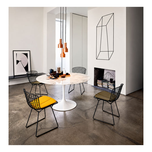 Harry Bertoia inspired wire dining chairs with black welded steel grid frames and colourful upholstered seat pads arranged around a round white marble Tulip pedestal dining table in a contemporary dining room, combining iconic mid-century modern design with sculptural elegance
