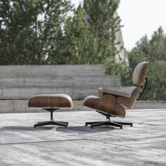 Eames-style lounge chair and matching pouf arranged on a patio beside greenery