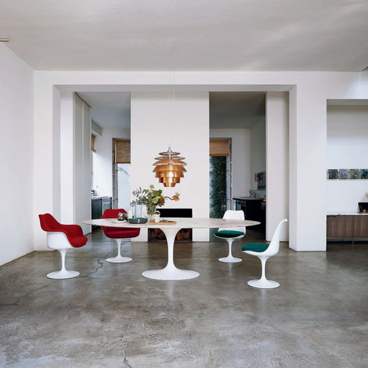 Round Tulip dining table with a white marble top and pedestal base paired with white Tulip dining chairs in red, green and white upholstery in a spacious contemporary dining room, inspired by Eero Saarinen's iconic mid-century modern Pedestal Collection.