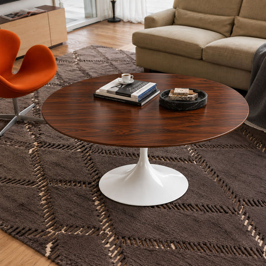 Walnut Prestige Tulip coffee table featuring a premium American walnut veneer round tabletop paired with a glossy white tulip pedestal base. Styled in a contemporary living room with a beige sofa, orange accent chair, textured rug, books, coffee cup, and decorative tray, showcasing timeless Italian design for modern, Scandinavian, mid-century, and minimalist interiors.
