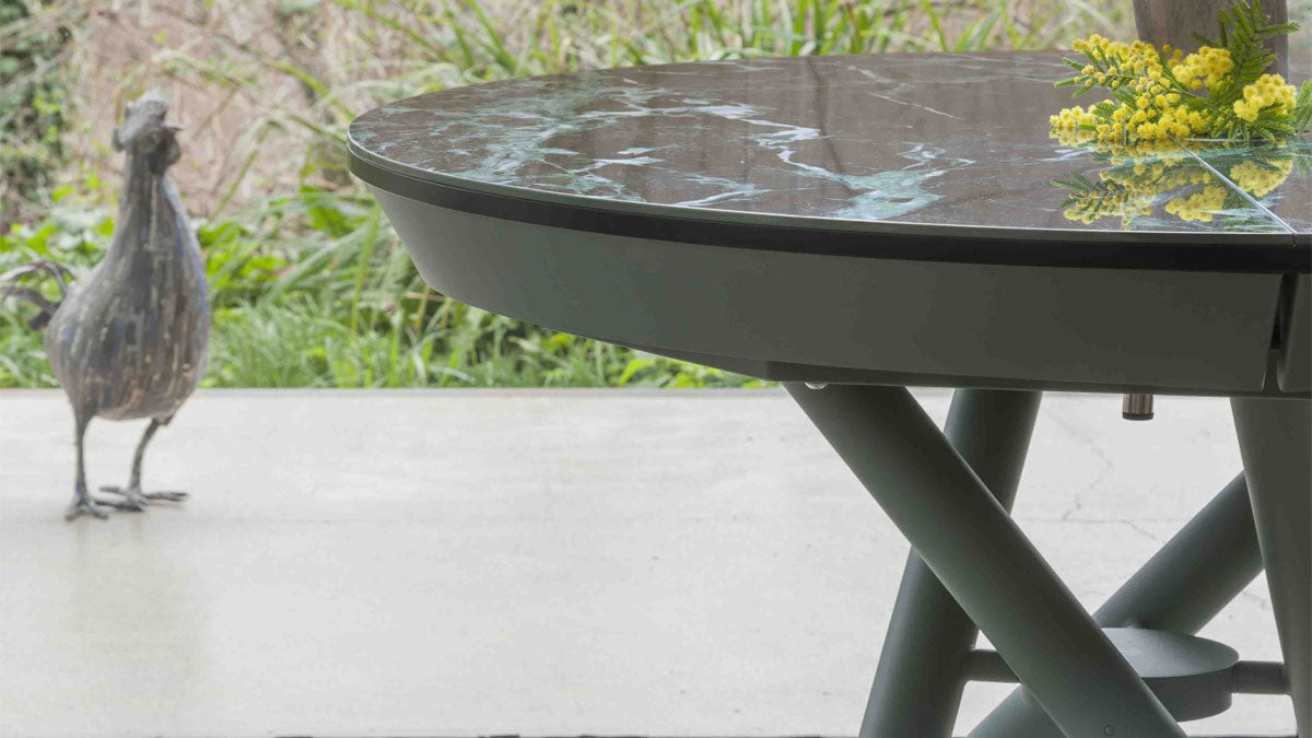 Close-up of Helios round transforming table showing green marble-effect top and painted metal crossed-leg base