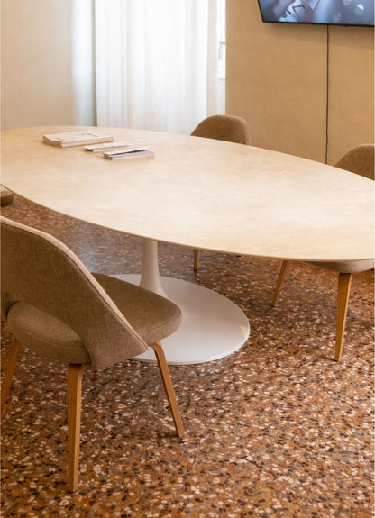 Oval tulip dining table with beige stone top and white pedestal base in a modern interior setting