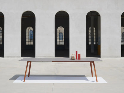 SCAB Squid outdoor extendable table with slim HPL top and terracotta aluminium legs, displayed in a contemporary architectural courtyard to showcase its Italian minimalist design.