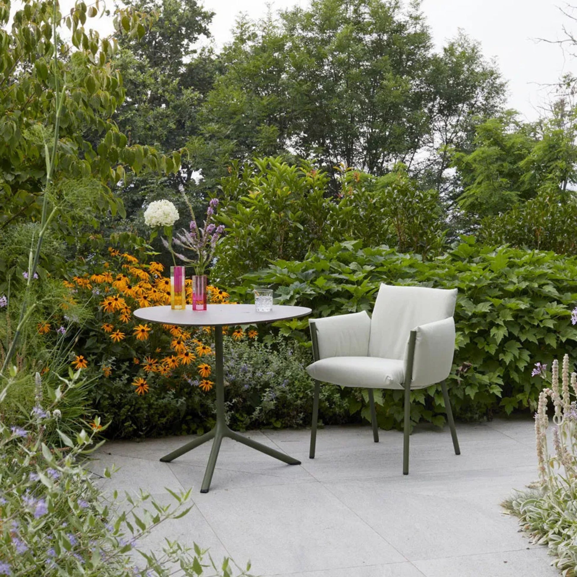 SCAB Tripè round outdoor bistro table with an olive green powder-coated aluminium base, paired with a lounge armchair in a contemporary garden patio setting, ideal for cafés, hotels and residential terraces.