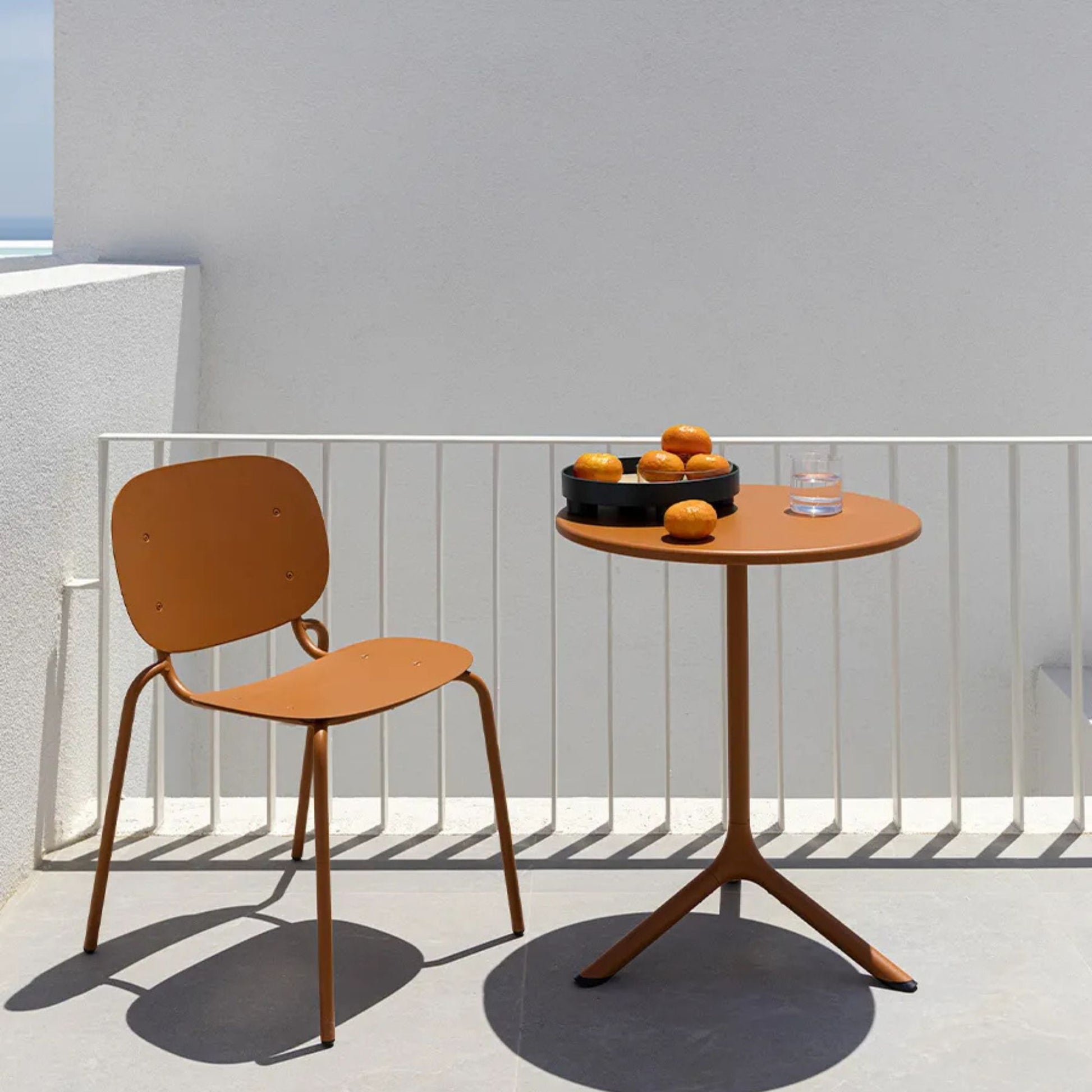 SCAB Tripè round outdoor side table with a terracotta aluminium pedestal base and matching tabletop, styled on a contemporary balcony for compact outdoor dining and café seating.