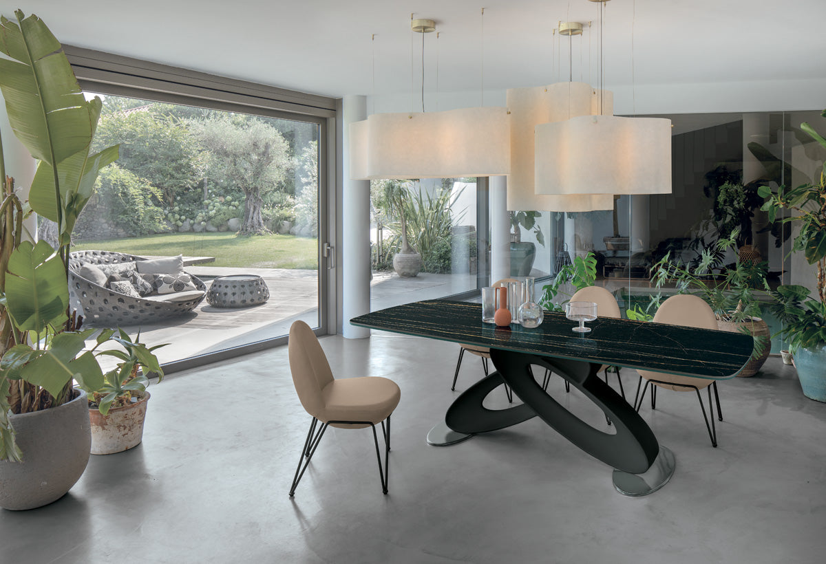 Eclipse Fixed Dining Table by Target Point with a black sculptural base and dark barrel-shaped tabletop in a contemporary Italian dining room overlooking a garden.