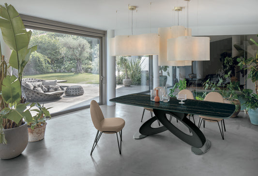 Eclipse Fixed Dining Table by Target Point with a black sculptural base and dark barrel-shaped tabletop in a contemporary Italian dining room overlooking a garden.