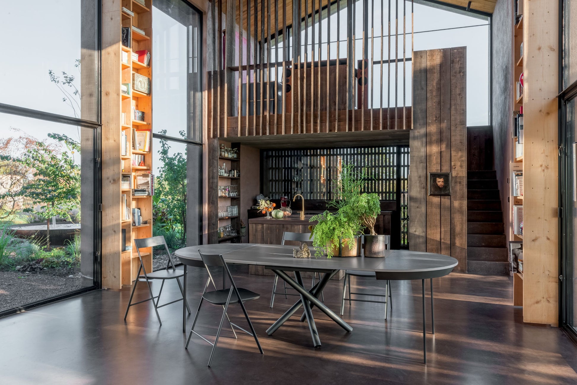 Modern kitchen and dining area with large windows, wooden walls, and a round table.