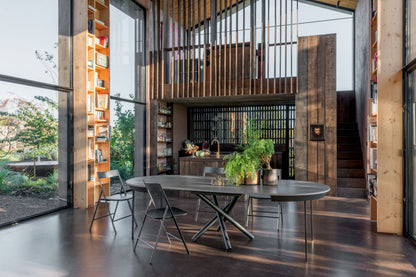 Modern kitchen and dining area with large windows, wooden walls, and a round table.