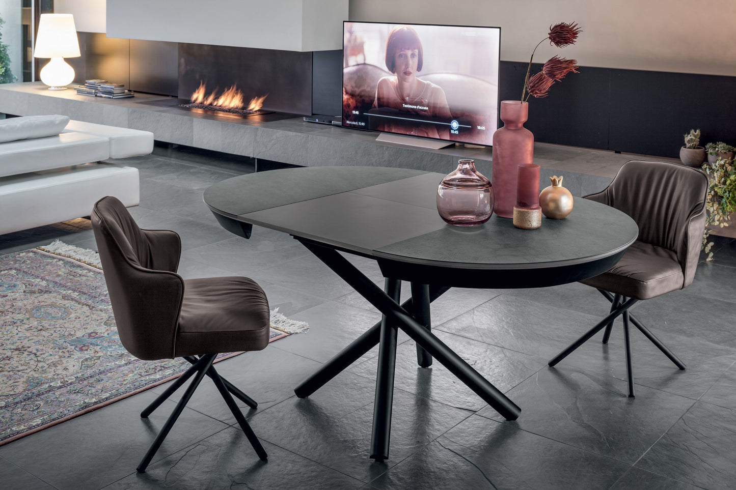 Modern living room with a round table, chairs, and a TV displaying a woman.