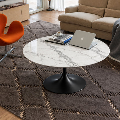 Arabescato Noir Tulip coffee table featuring a polished Arabescato marble tabletop with striking grey veining, paired with a matte black tulip pedestal base. Styled in a contemporary living room with a beige sofa, orange accent chair, textured rug, books, coffee cup, and laptop, creating a sophisticated Italian-inspired workspace and lounge. Ideal for modern, Scandinavian, minimalist, and mid-century interiors.