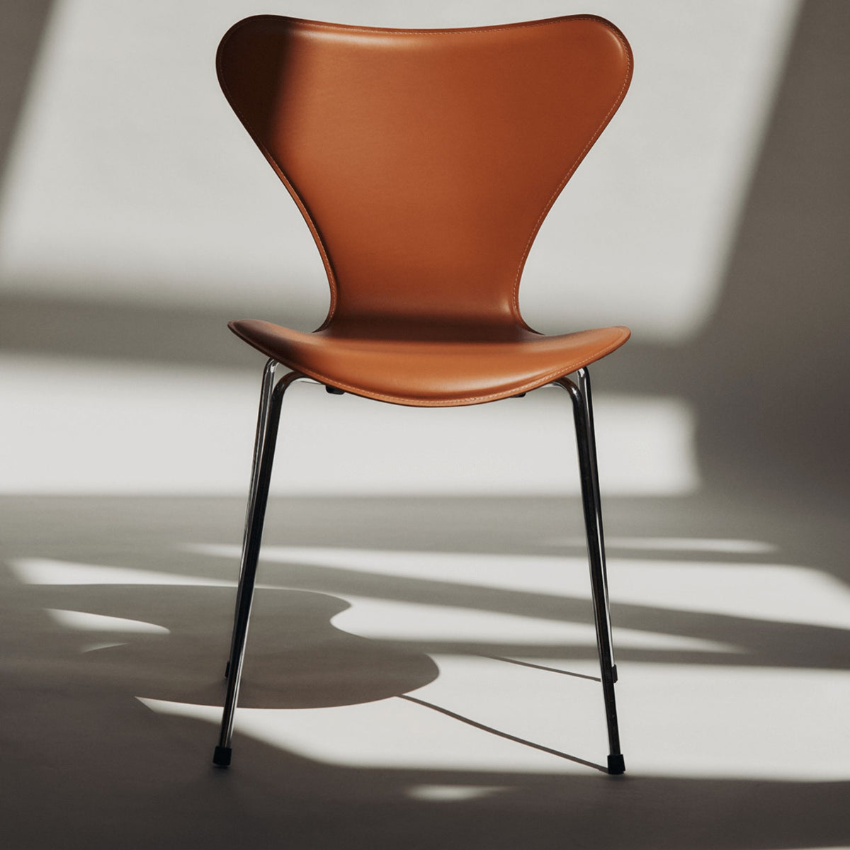 Arne Jacobsen inspired brown leather dining chair with black powder-coated steel legs, featuring a sculptural curved backrest for modern Italian dining rooms and contemporary interiors.