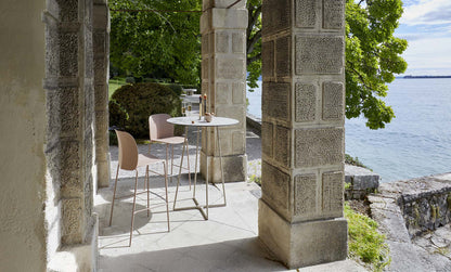 S•CAB Atomo Bistro Table Base with a round tabletop and matching bar stools in an elegant outdoor terrace overlooking the water.