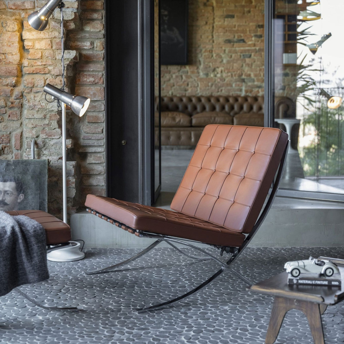 Barcelona Chair upholstered in cognac brown tufted leather with a polished chrome frame, displayed in a contemporary industrial-style living room, offering iconic modern lounge seating for luxury residential and commercial interiors.