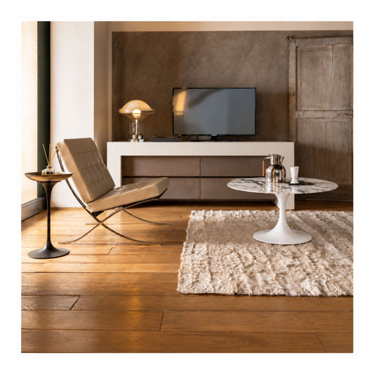 Barcelona lounge chair paired with a white marble Tulip high side table featuring a round marble top and white pedestal base in a contemporary living room with warm wood flooring.