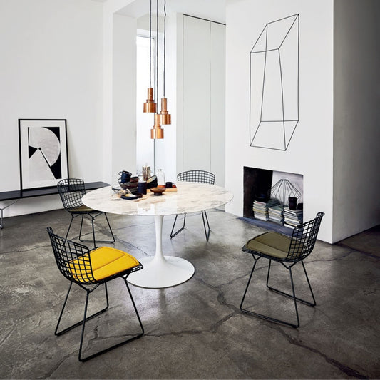Harry Bertoia inspired wire dining chairs with black welded steel grid frames and colourful upholstered seat pads arranged around a round white marble Tulip pedestal dining table in a contemporary dining room, combining iconic mid-century modern design with sculptural elegance