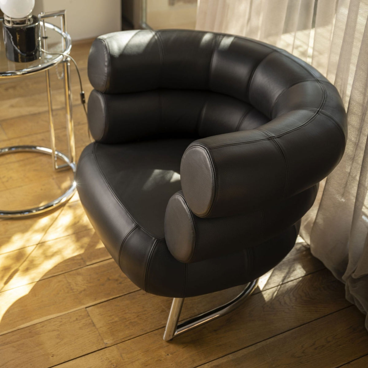 Close-up view of a Bibendum armchair upholstered in black leather with a polished chrome tubular steel frame, showcasing its iconic cylindrical cushioned backrest and armrests for luxury modern living rooms, hotel lounges and contemporary designer interiors