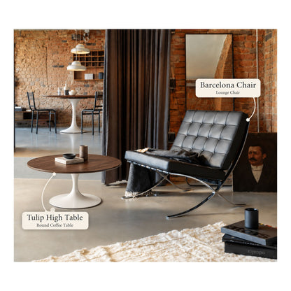 Black Barcelona lounge chair paired with a walnut round Tulip coffee table featuring a white pedestal base in a contemporary loft living room with exposed brick walls and modern décor.