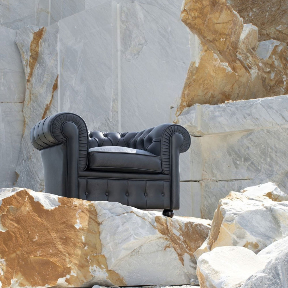 Black Chesterfield leather armchair with deep button tufting, rolled arms, and a luxurious contemporary design, displayed against a natural marble stone backdrop