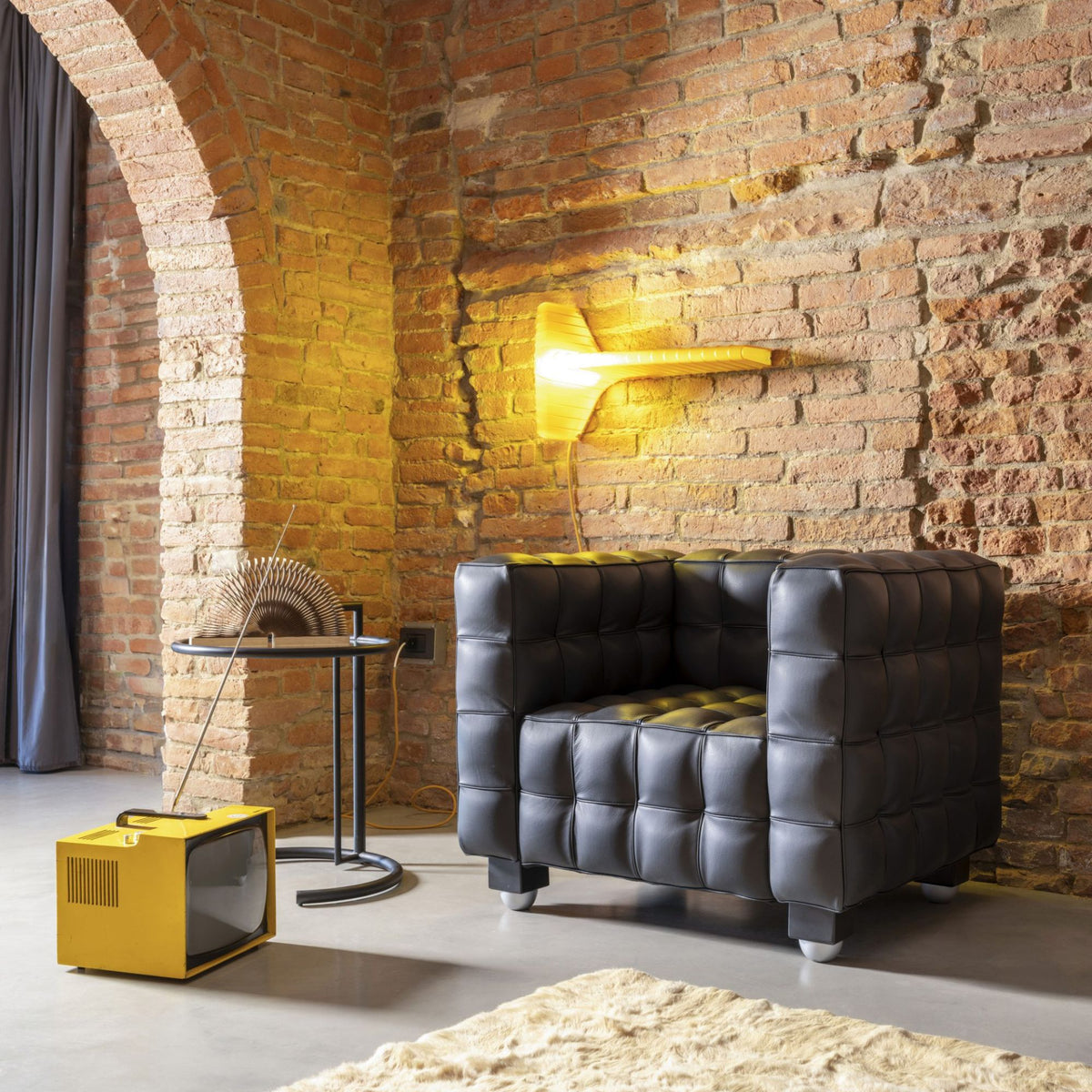 Black tufted leather cube armchair with deep button quilting in a contemporary loft interior, featuring a bold geometric silhouette inspired by iconic Italian modernist lounge furnitur