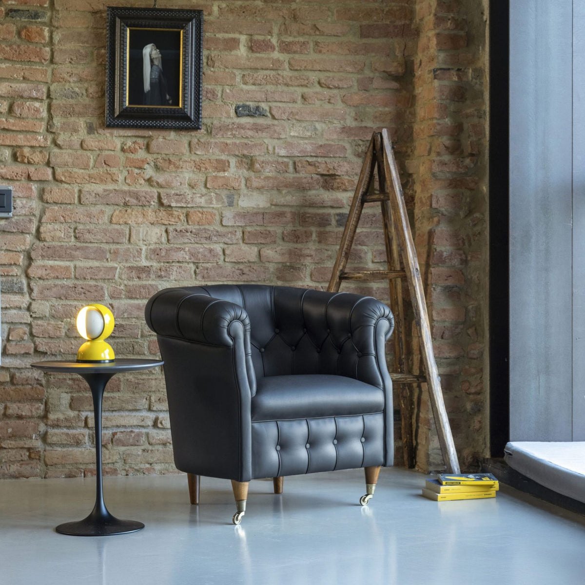 Black leather Chesterfield tub armchair with rolled arms, button-tufted back, smooth seat cushion, tapered wooden legs and brass castors, ideal for luxury living rooms, offices and reading spaces.