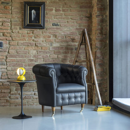 Black leather Chesterfield tub armchair with rolled arms, button-tufted back, smooth seat cushion, tapered wooden legs and brass castors, ideal for luxury living rooms, offices and reading spaces.