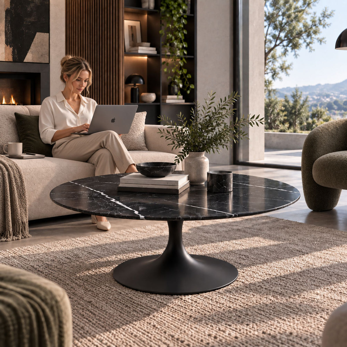 Woman working on a laptop beside a black marble-effect oval Tulip coffee table with a black pedestal base in a contemporary luxury living room.