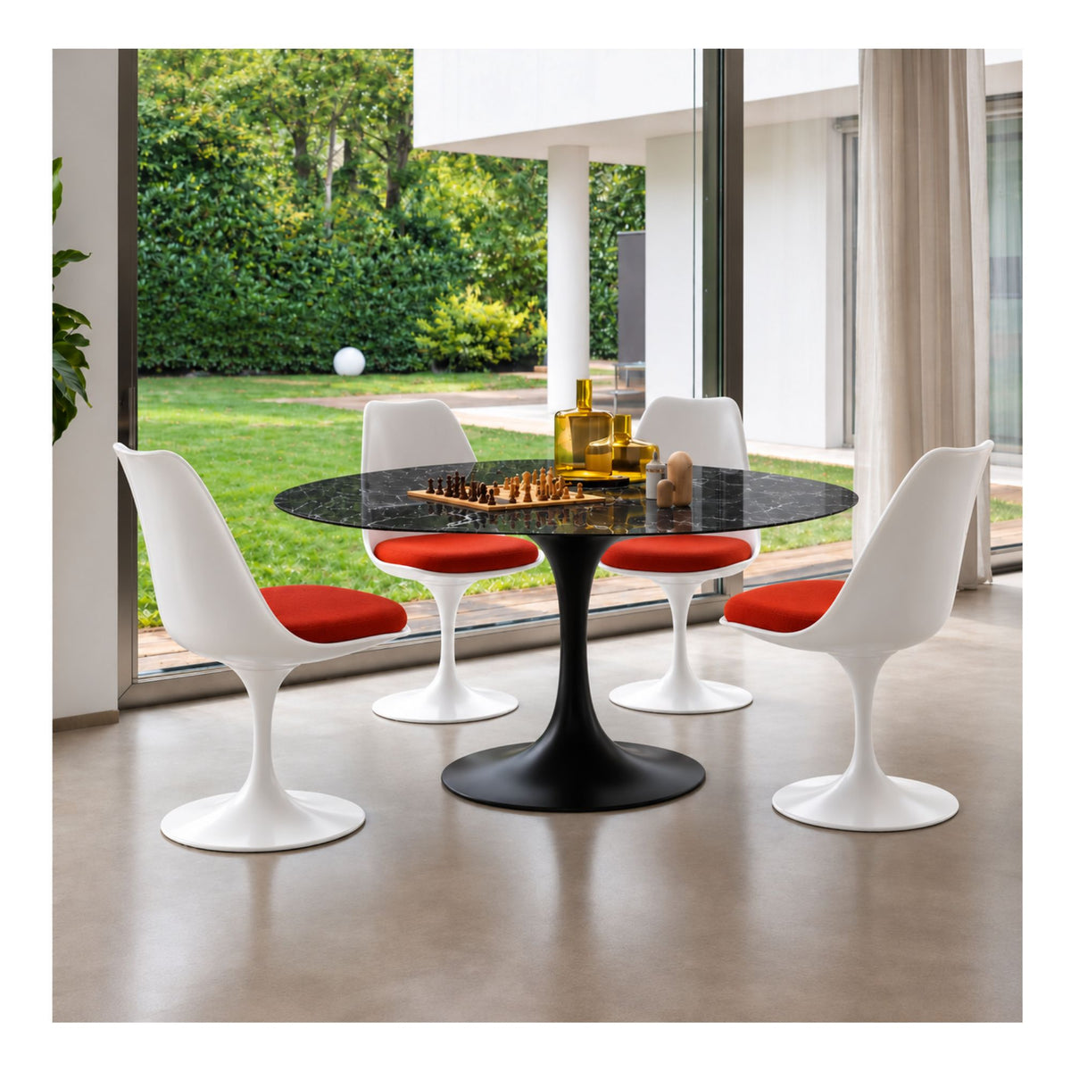 Black marble round Tulip dining table with a black pedestal base paired with four white Eero Saarinen Tulip dining chairs featuring red upholstered seat cushions in a modern dining room.
