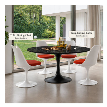 Black marble round Tulip dining table with a black pedestal base paired with four white Eero Saarinen Tulip dining chairs featuring red upholstered seat cushions in a modern dining room.