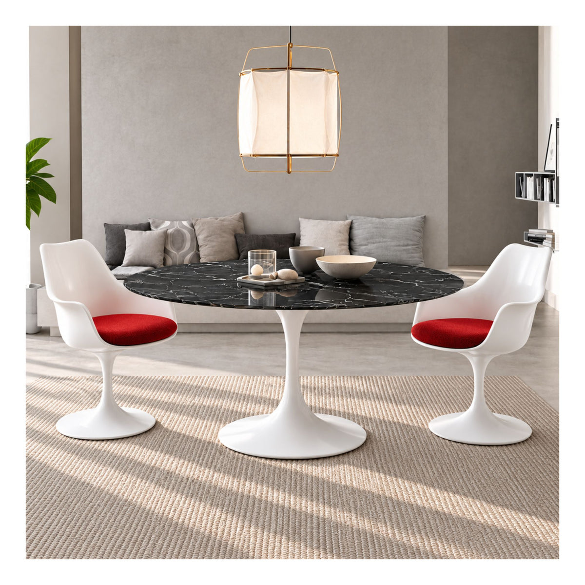 Black marble round Eero Saarinen Tulip dining table with a white pedestal base paired with two white Tulip armchairs featuring red upholstered seat cushions in a contemporary living and dining space.