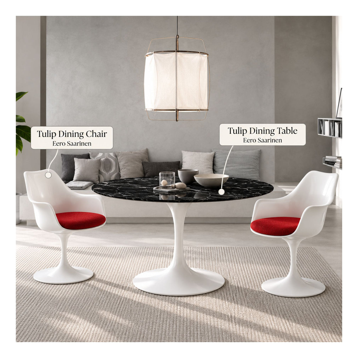 Black marble round Eero Saarinen Tulip dining table with a white pedestal base paired with two white Tulip armchairs featuring red upholstered seat cushions in a contemporary living and dining space.