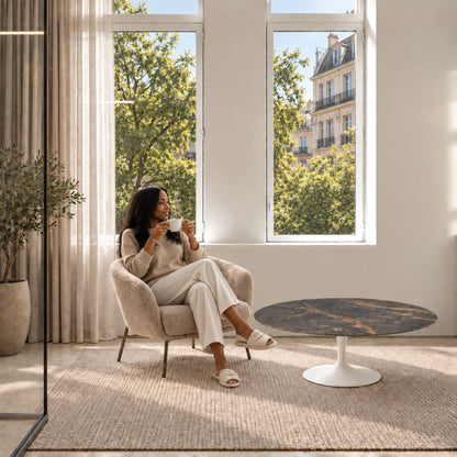 Bronze Eclipse Tulip coffee table featuring a polished Bronze Noir marble tabletop with dramatic bronze and ivory veining, paired with a glossy white tulip pedestal base. Styled in a bright contemporary living room with a modern lounge chair, large windows, and warm natural daylight. A luxury Italian designer coffee table for sophisticated modern interiors.