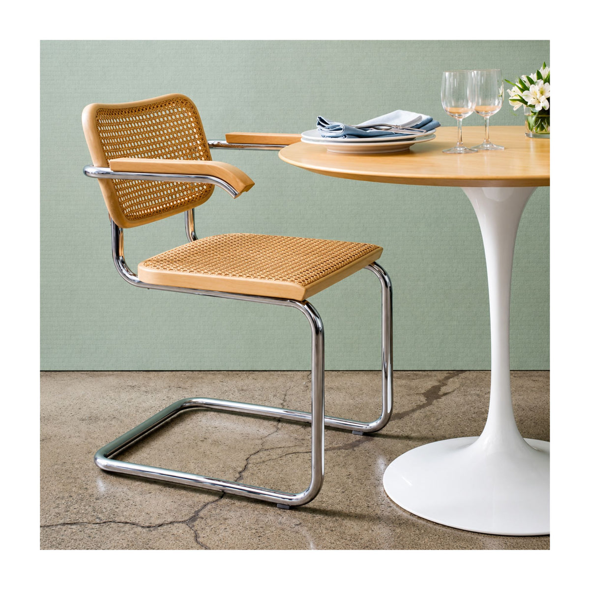 Marcel Breuer Cesca cane armchair with natural woven cane seat, wooden armrests, and polished chrome cantilever frame paired with a white Saarinen Tulip dining table in a contemporary dining room.