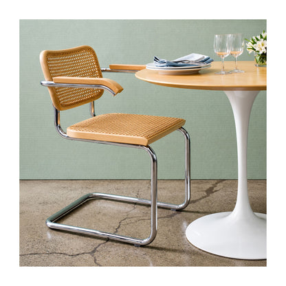 Marcel Breuer Cesca cane armchair with natural woven cane seat, wooden armrests, and polished chrome cantilever frame paired with a white Saarinen Tulip dining table in a contemporary dining room.