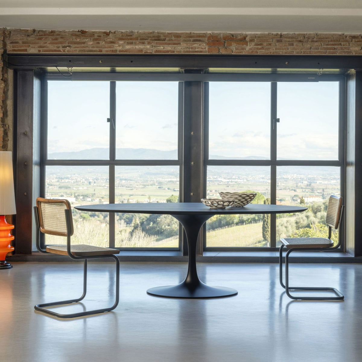 Marcel Breuer Cesca cane dining chair featuring a natural woven cane seat and back with a black frame and cantilever tubular steel base in a modern dining room overlooking large windows.