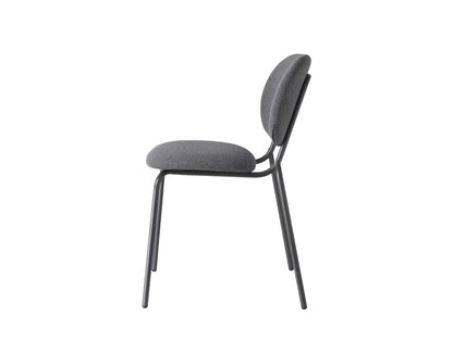 Side view of a charcoal upholstered dining chair with a rounded backrest, padded seat, and slim dark metal frame.