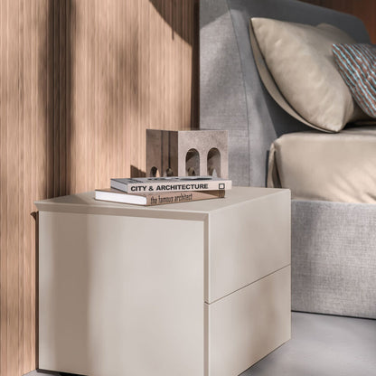 Beige nightstand with books next to a bed in a bedroom setting