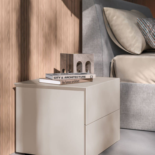 Beige nightstand with books next to a bed in a bedroom setting