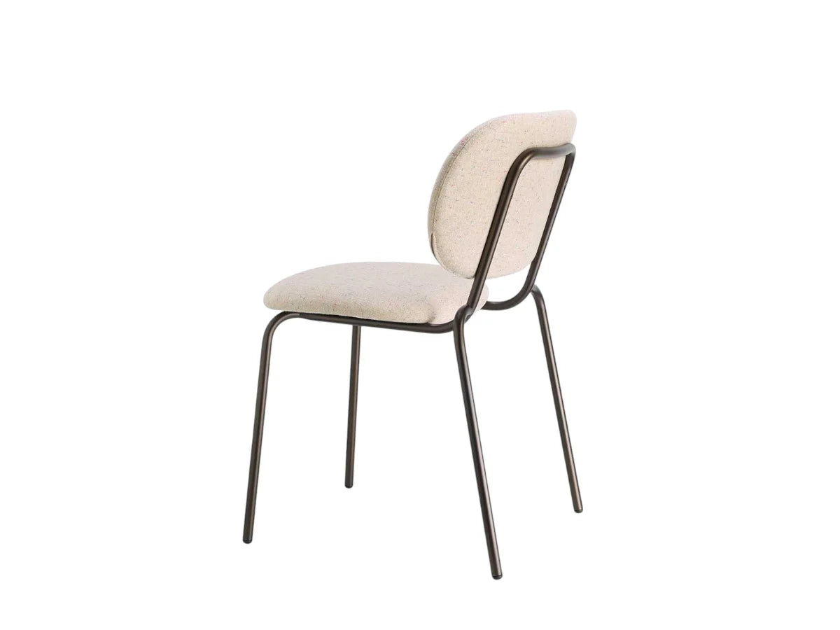 Rear angled view of a cream upholstered dining chair with a curved backrest, padded seat, and slim dark metal frame.