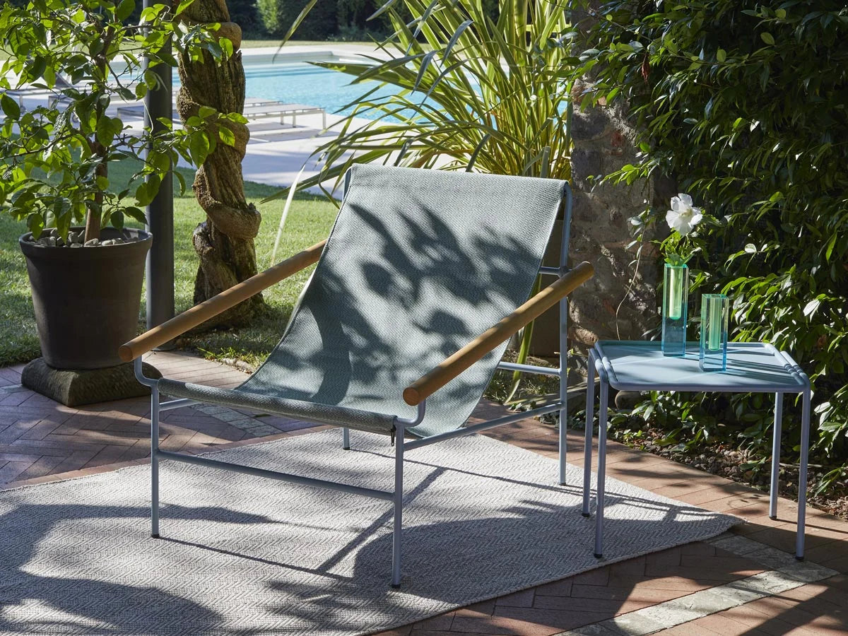 Dress Code Glam 2582 lounge chair with a blue-grey sling fabric seat and wooden armrests on a modern outdoor patio.