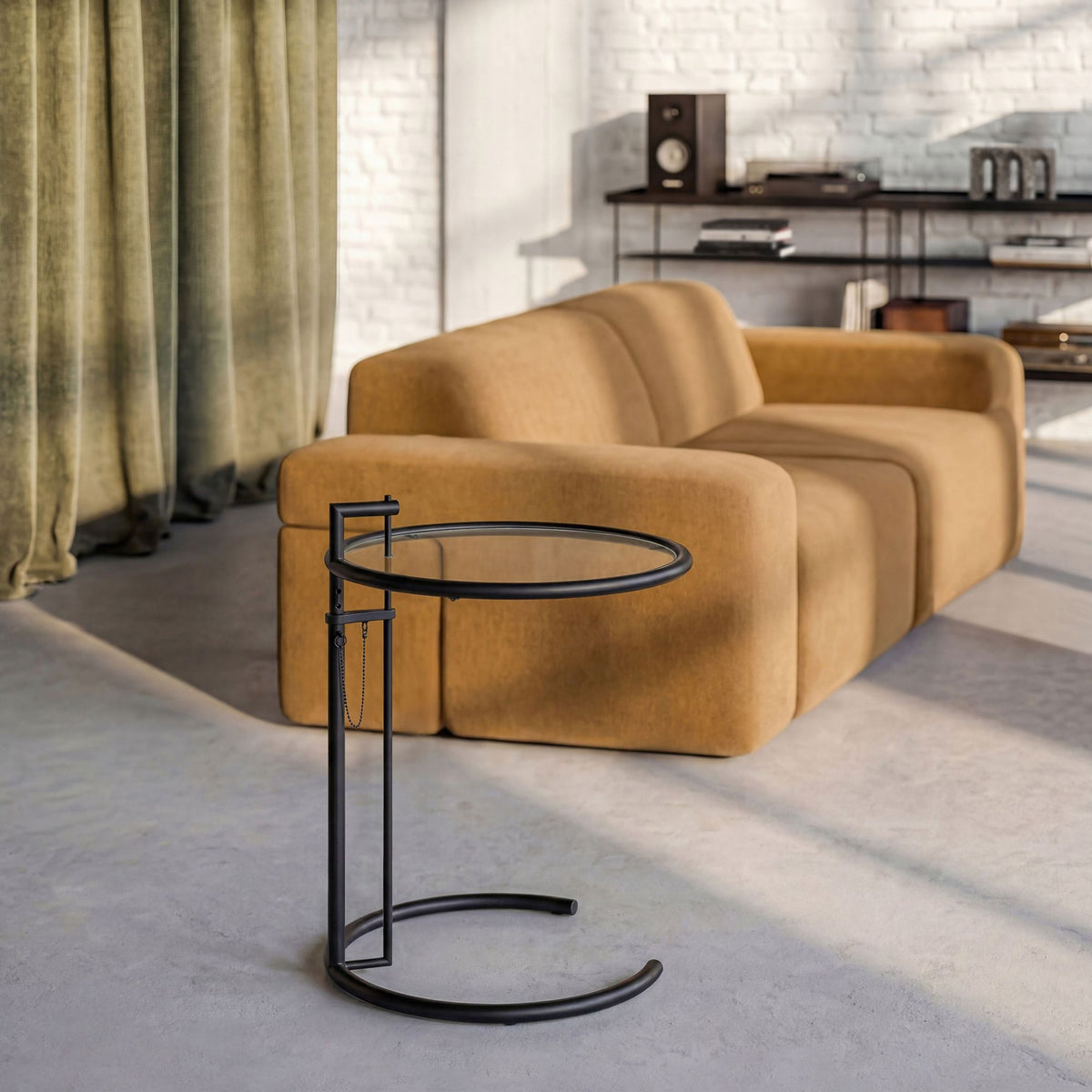 Eileen Gray E1027 black adjustable side table with a circular glass top and matte black tubular steel frame, styled beside a contemporary mustard sofa in a modern living room, showcasing a timeless designer accent table for luxury interiors.