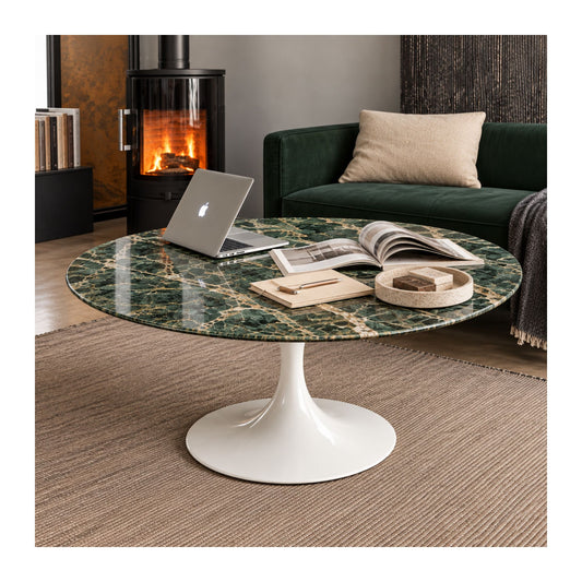 Emerald Prestige Tulip coffee table featuring a polished Alpi Green marble tabletop with striking white veining, paired with a glossy white tulip pedestal base. Styled in a contemporary living room with a green velvet sofa, wood-burning fireplace, laptop, books, and decorative accessories, creating a sophisticated Italian-inspired workspace and lounge. Ideal for modern, Scandinavian, luxury, and mid-century interiors.
