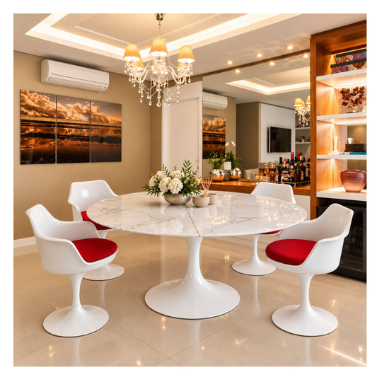 Extendable round Tulip dining table with a white veined ceramic top and pedestal base, surrounded by white chairs with red seat cushions.