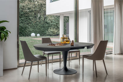 Modern dining room with a round black table and chairs near large windows.