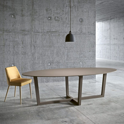 Italian oval taupe dining table with a geometric metal base in a modern minimalist dining room with a concrete interior.