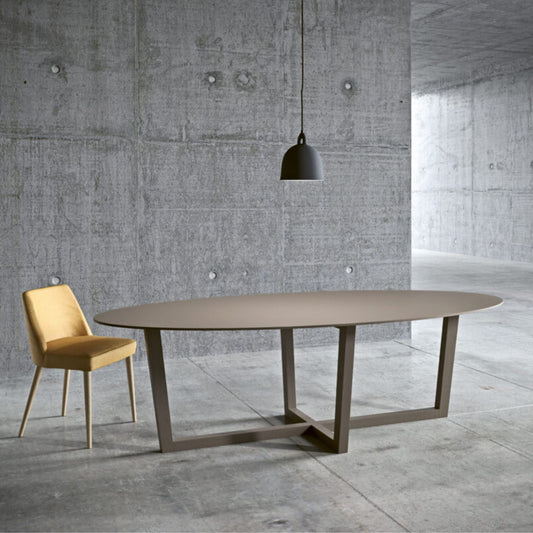 Italian oval taupe dining table with a geometric metal base in a modern minimalist dining room with a concrete interior.