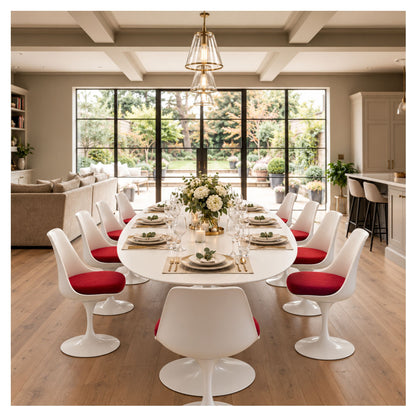 Large oval Tulip executive table with a white top and pedestal base, set for dinner and surrounded by white chairs with red seat cushions.