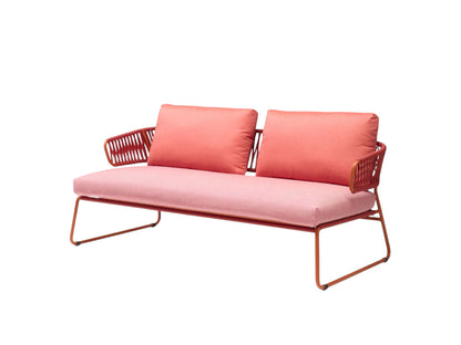 Front angled view of the Lisa Club outdoor sofa with coral upholstered cushions, woven armrests, and a matching metal frame.