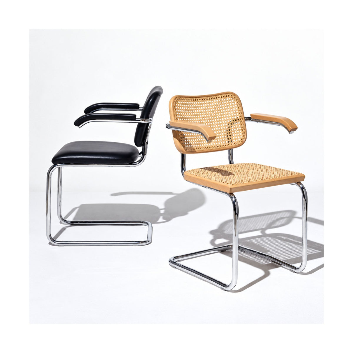 Marcel Breuer Cesca armchair collection featuring a natural cane armchair with wooden armrests beside a black upholstered leather cantilever armchair, both with polished chrome tubular steel frames on a white background.